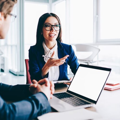 Businesswoman in blue blazer and glasses enhancing client relationships during meeting in windowed conference room.