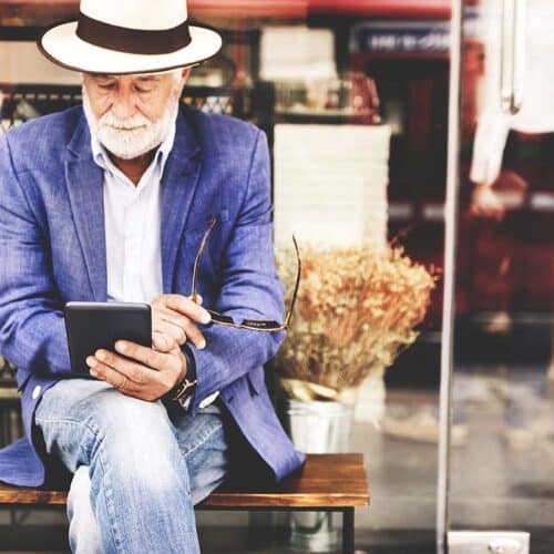 Older adult sitting on a bench reading on a tablet.