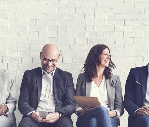 Row of professionals seated in front of a white brick wall.